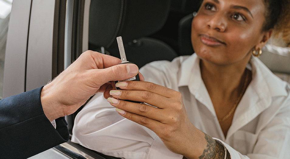 Women getting handed keys while sitting in her car